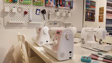 Sewing machines sit on a table in a creative space.