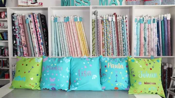 Colourful cushions stand in front of a fabric shelf in a sewing room.