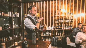 Man presents bottle in a cozy bar setting.