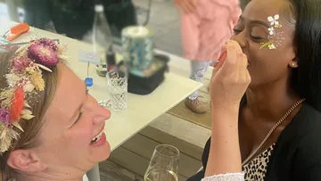 A woman is applying makeup to another woman in a festive setting.