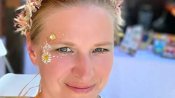 Woman with floral face painting and flower hair accessories smiles.