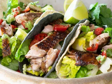 Three tacos with chicken, lettuce, tomatoes, and lime.