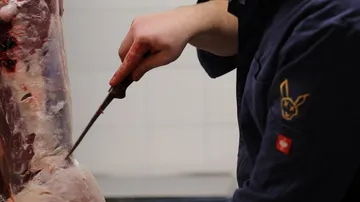 Ein Mensch schneidet Fleisch in einer Metzgerei.