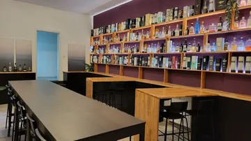 Bar mit Regalen voller Spirituosen vor minimalistischer Sitzgelegenheit.