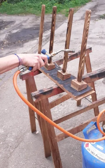 Hand holds burner outside while wood supports are being treated