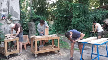 Holzarbeiter bearbeiten Holzstücke in einem grünen Außenbereich.