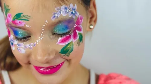 Girl with colorful flower face painting smiles happily.