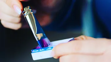 Brush dips into paint to paint on a palette.