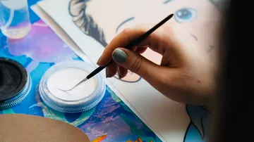 A hand paints on a picture with a brush.