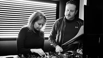 Two DJ's work on a mixer in a studio at the same time.