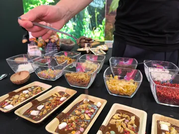 Spoon lifts chocolate over various ingredients at a table.
