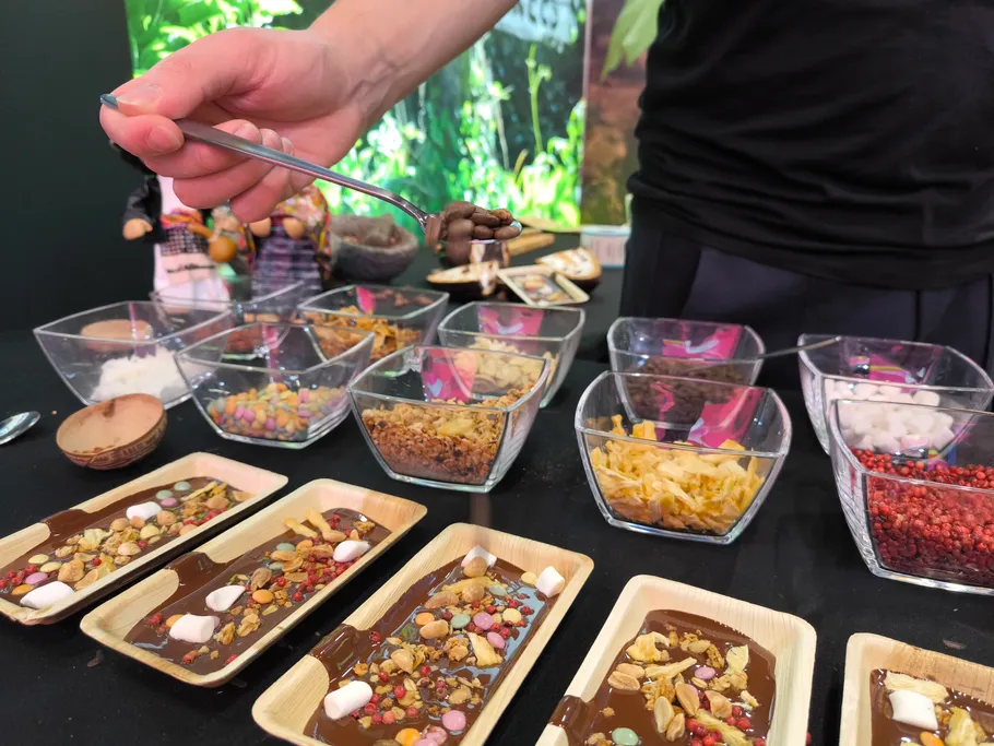 Spoon lifts chocolate over various ingredients at a table.