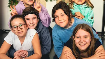 Sechs Kinder posieren lächelnd für ein Gruppenfoto zusammen.