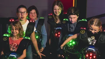 Sechs Kinder tragen Laser-Tag-Westen und lachen.
