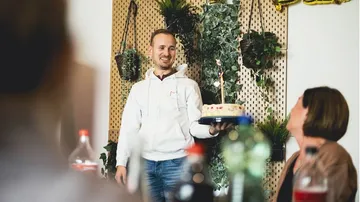 Mann mit Kuchen feiert Geburtstag im dekorierten Raum.
