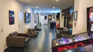 Lange Halle mit Sitzgelegenheiten und einem Flipperautomaten.