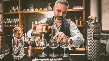 Bartender pours drink into three glasses at the bar.