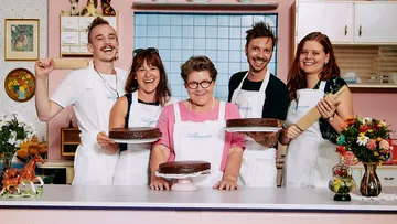 Fünf Personen präsentieren Kuchen in einer freundlichen Küche.