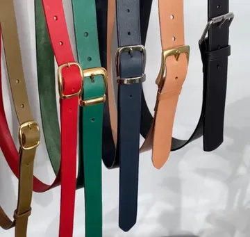 Leather belts hang on a wall in different colors.