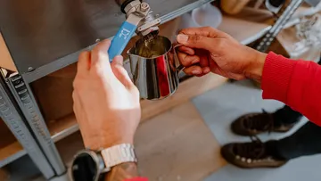 A person taps wax into a measuring cup.