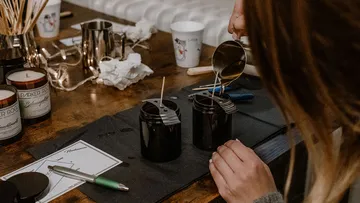 Two candles are filled with wax in a workshop.