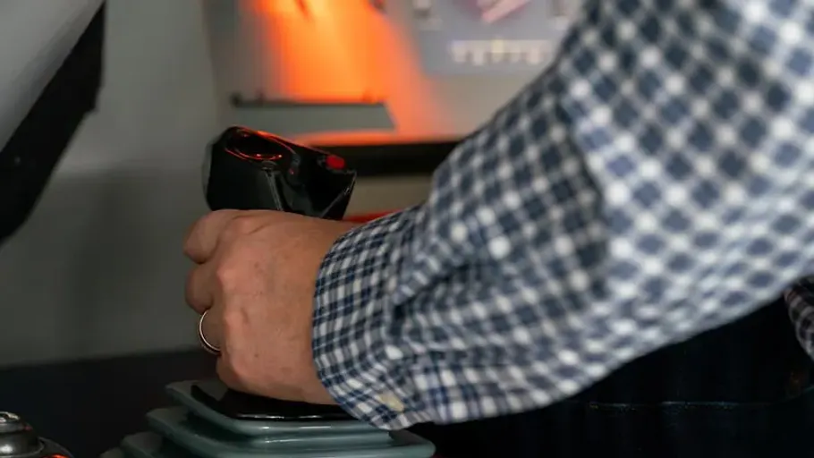 Hand greift einen Joystick in einem cockpitähnlichen Raum.