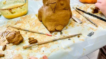 Clay figure of an owl's head is modeled on a table.