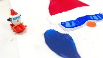 Eine Figur mit Weihnachtsmütze steht neben einem Bild.