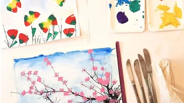 Acrylic paints and brushes lie on a table with pictures.