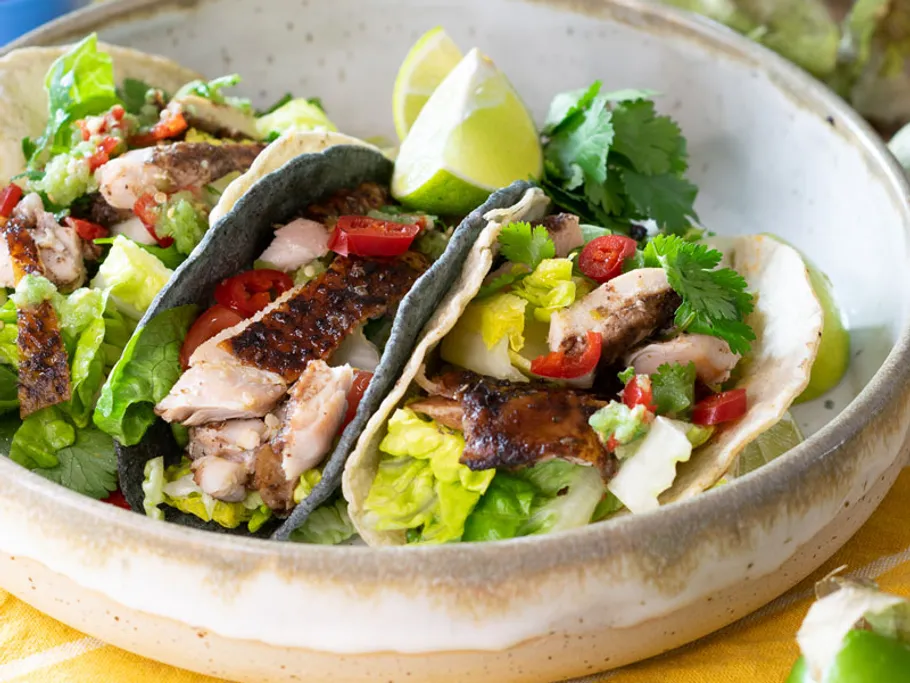 Drei Tacos mit Hähnchen, Gemüse und Limettenscheiben in Schüssel.