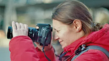 Frau mit Kamera fotografiert an einem unscharfen Hintergrund.