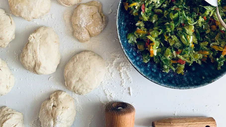 Teigstücke liegen auf einer bemehlten Fläche, während Salat vorbereitet wird.