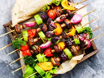 Gemüsespieße liegen auf einer Holzplatte mit Salat.