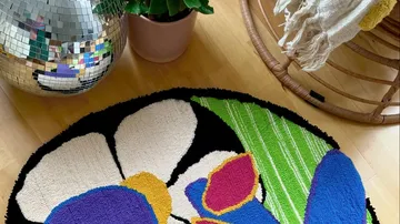 Bunter Teppich liegt auf einem Holzboden, umgeben von Pflanzen.