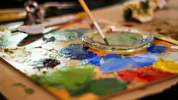 Palette mit Farben und Pinsel auf einem Tisch.