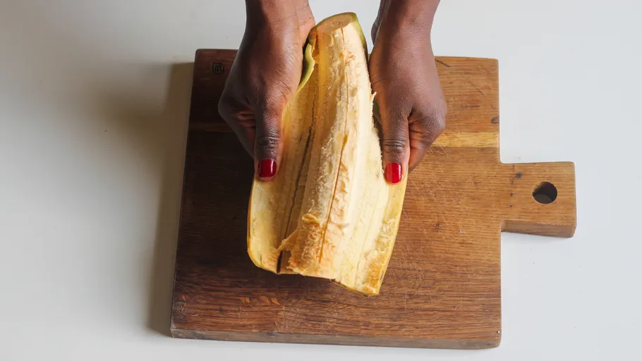 Hands peeling plantain on wooden board.