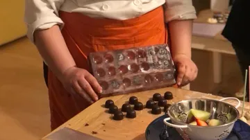 Person hält eine Schokoladenform über Pralinen auf Tisch.
