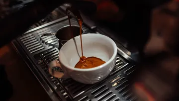 Kaffeewasser fließt in eine weiße Tasse auf einer Maschine.