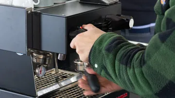 One hand operates a coffee machine in a barista environment.