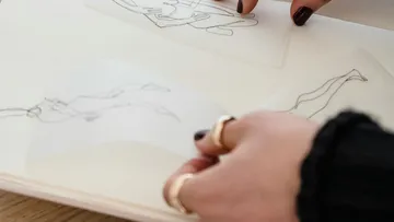 Eine Hand hält durchsichtige Folien über Zeichnungen in einem Buch.