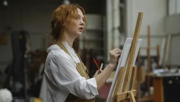 Künstlerin malt konzentriert auf eine Leinwand im Atelier.