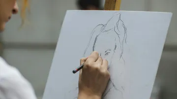 Eine Person zeichnet einen Skizze auf einer Leinwand.