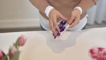 Hands hold a flower while a person crafts.