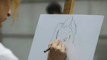Eine Person skizziert ein Porträt auf einer Leinwand.