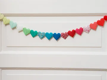 Bunte Papierherzen hängen an einer weißen Wand.