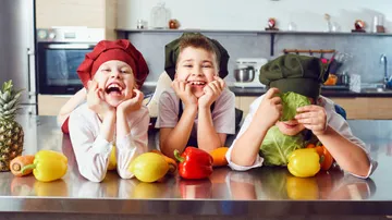 Three children laugh as they present fresh vegetables.