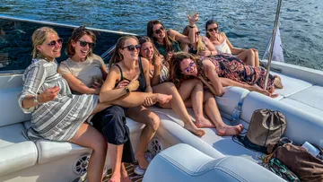 Acht Frauen entspannen auf einem Boot und lachen zusammen.
