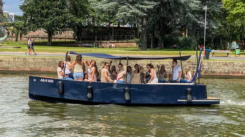 Group on a boat cruising a river, park background.