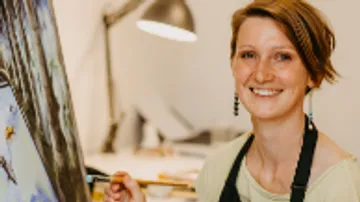 Woman painting on canvas in a studio with a smile.