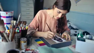 Frau malt konzentriert auf Papier in kreativem Raum.